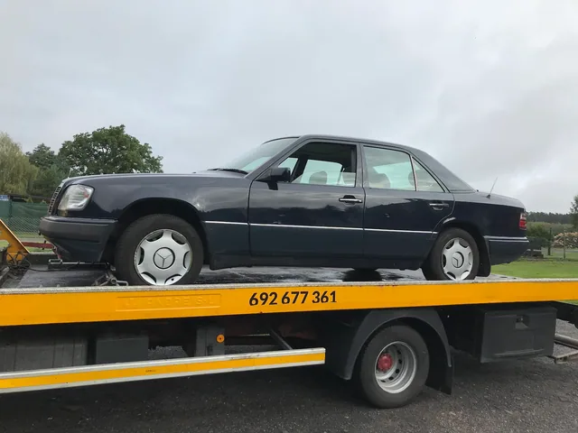 Czarny Mercedes W124 na platformie żółtej lawety z numerem 692 677 361