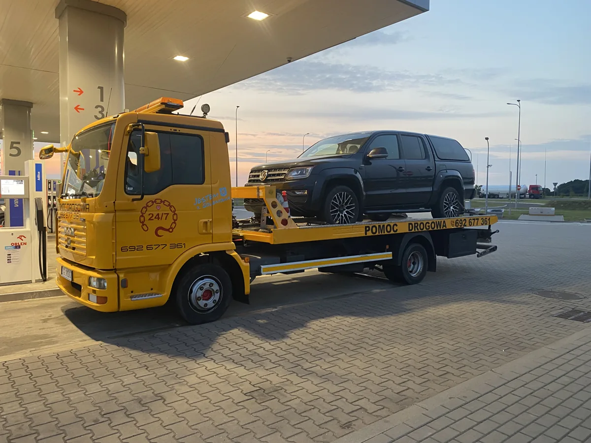 Żółty MAN TOPHOL z czarnym VW Amarokiem na stacji paliw o zmierzchu